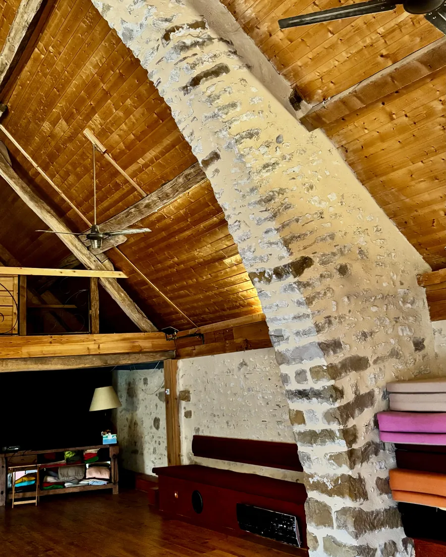 La salle de pratique sous la charpente : plafond de bois, pilier de pierre, parquet et coussins